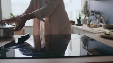 Tanımlanamayan bir kadının elektrikli ocağa soğuk suyla tava koyup ev mutfağında yemek pişirme sürecinin keyfini çıkarması.