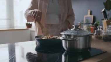 Tanımlanamayan bir kadının iç mutfakta spagetti sosu yaparken, sosu karıştırırken ve ocakta kaynar suyu kontrol ederken görüntüsü.