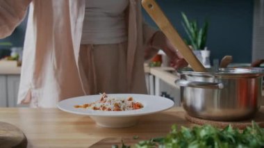 Beyaz tabakta spagetti bolonezinin üstüne rendelenmiş parmesan ve doğranmış bitkiler serpiştiren tanınmamış bir kadın resmi.