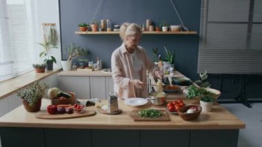 Orta boy beyaz kadın spagetti servis ederken beyaz tabak üzerinde ahşap kaşık ve çatalla pişirilmiş, mutfak tezgahında sıcak ve rahat bir şekilde dururken.