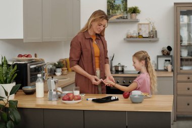 Glikoz seviyelerini izlemek için kan testi şeritleri kullanan ve diyabetli çocuğa bakan bir kadının yan görüş portresi. 