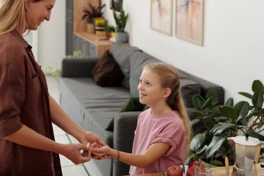 Diabet hastası küçük bir çocuğa bakan ebeveynin portresi. Kızı, evde dikilirken annesinin glikoz seviyelerini gözlemlemesine gülümsüyor. 