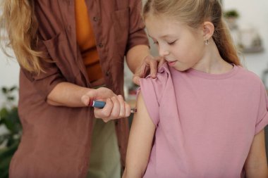 Kollarında diyabet tedavisine yardımcı olan genç kızına insülin enjekte eden tanınmayan bir anneye yakın çekim.