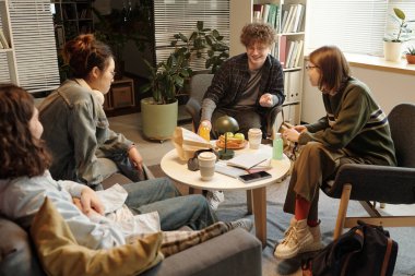 Yüksek açı, sohbet eden bir grup öğrencinin rahat çalışma odasındaki masasında loş ışıklarla aydınlatıldığını gösteriyor.