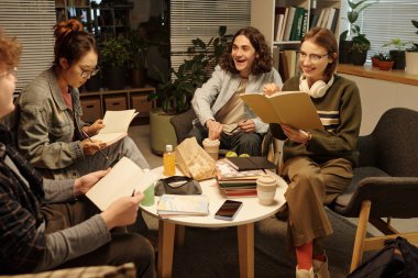 Bir grup genç birlikte ders çalışıyor rahat bir okul salonunda düşük ışık ve gülümsemeyle oturuyor.