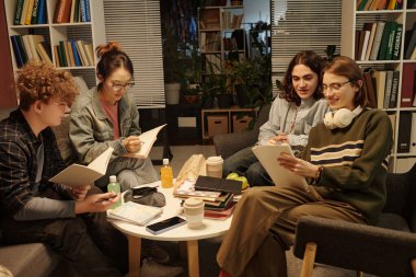 Sınavlarda birlikte çalışan genç öğrencilerin hoş bir sahnesi. Okul salonunda, ışık az ve gülümseyerek oturuyorlar.