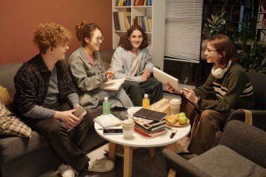 Neşeli gençlerden oluşan bir grubun yüksek açılı görüntüsü rahat kütüphane salonunda düşük ışıkta oturuyorlar.