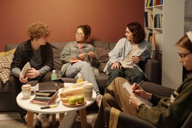 Bir grup genç, rahat kütüphane salonundaki kanepede düşük ışıklandırmayla oturuyor.