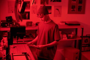 Karanlık odada, yaratıcı stüdyo fotokopi odasında genç fotoğrafçı tarafından aydınlatılan fotoğraflara bakan genç bir çocuğun belden yukarı portresi.