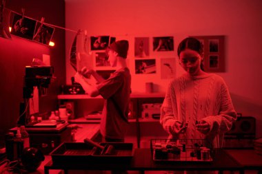 İki genç fotoğrafçı birlikte karanlık odada çalışıyor. Elinde ön planda film ruloları tutan genç bir kız tarafından aydınlatılıyor. Yaratıcı analog fotoğrafçılık süreci uzayı kopyalıyor.