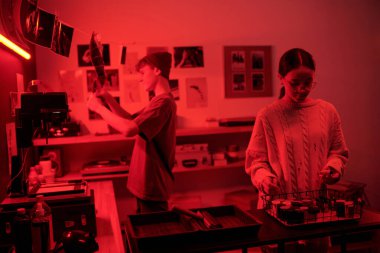 İki genç fotoğrafçının portresi, karanlık odada kırmızı neon ışıklı analog fotoğrafçılık ile aydınlatılan fotoğraf baskıları üzerinde çalışıyor.