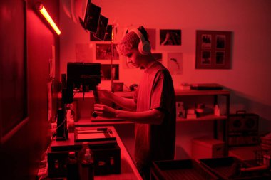 Yaratıcı süreçte genç fotoğrafçıların yan görünüm portresi. Kulaklıkla müzik dinlerken, karanlık odada kırmızı ışık fotokopi alanı tarafından aydınlatılan film geliştiriliyor.