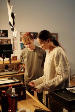 Yaratıcı fotoğrafçılık projesinde çalışan iki gencin dikey yan görüş portresi stüdyoda negatifleri geliştiriyor.