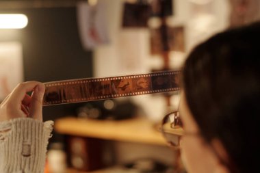 Karanlık odada fotokopi için fotoğraf seçerken genç bir kızın elinde ışığa negatifleri tuttuğu omuz üstü.