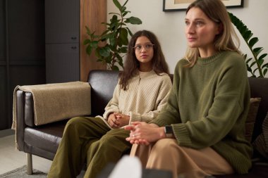 Aile terapisi sırasında rahat bir ofiste psikologla annesine bakan genç bir kızın portresi.