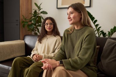 Gülümseyen anne ve kızın aile terapisi sırasında koltukta oturup psikoloğu dinlemesinin yan görüntüsü.