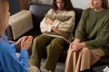 Terapi seansında anne ve kızıyla konuşurken nazik davranan şefkatli kadın terapistin omzunun üstünden. Ellere odaklan, kopyalama alanına odaklan.