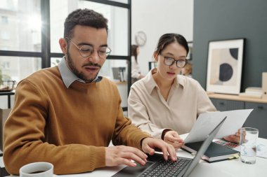 Genç Ortadoğulu bir adamın portresi. İş arkadaşlarıyla görüşüyor ve ofiste dizüstü bilgisayar kullanıyor.