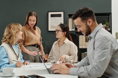 Genç iş adamları ofiste gülen adamla iş birliği yapıyor. Önplanda dizüstü bilgisayar kullanıyorlar.