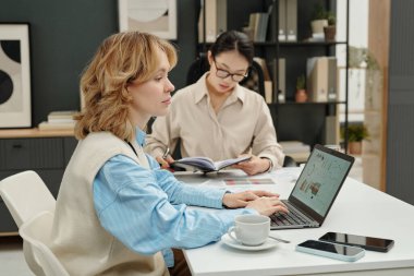 Bilgisayarla veri analiz eden genç iş kadınının arka plan fotokopi alanındaki meslektaşıyla yan görünüm portresi