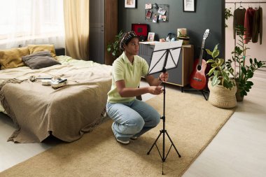 Gençler, doğal ışık ve müzik aletleriyle dolu rahat bir yatak odasında rahat bir ortam yaratmak için müzik sayfası hazırlıyorlar.