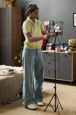 Genç siyahi kişi rahat oturma odasında duruyor sanatsal ekipmanları ayarlıyor ve yaratıcı projeye hazırlanıyor, odaklanmış ve kendini ifade ediyor.