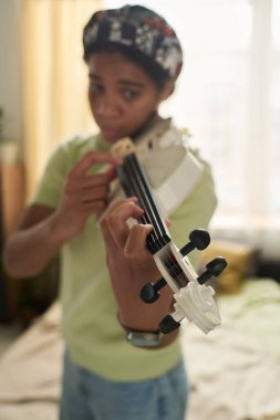 Ergen kemancı, iyi aydınlatılmış bir odada karmaşık bir şekilde detaylı bir keman çalmaya dalmış, gündelik giysiler giyiyor, müzik ve sanat tutkusunu sergiliyor.