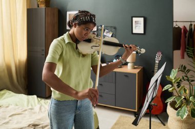 Dekorlu rahat bir yatak odasında nota okurken keman çalan genç bir kız. Sakin bir ortamda performansı mükemmelleştirmeye odaklan.