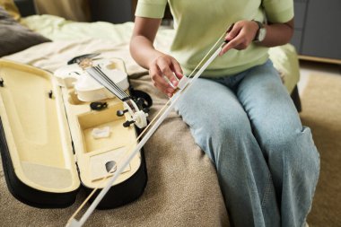 Yanında keman çantası açık, rahat bej koltukta otururken kemanı bağlayan kişinin yakın çekimi, detaylara ve işçiliğe dikkat gösteriyor