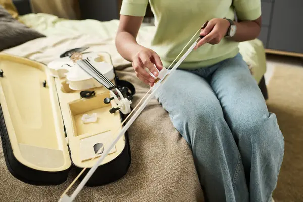 Yanında keman çantası açık, rahat bej koltukta otururken kemanı bağlayan kişinin yakın çekimi, detaylara ve işçiliğe dikkat gösteriyor