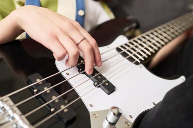 Otururken elektro gitarın tellerini koparan, gündelik kıyafetler giyen ve parmağında yüzük olan insanların yakın çekim görüntüsü. Resim göstergeleri enstrümanla detaylı etkileşim