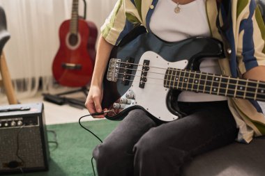 Oturma odasında akustik gitar çalan ve arka planda yükseltici bulunan kişi sıcak doğal ışıkla donanımlı müzikal atmosfer yaratıyor.