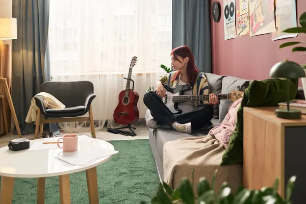 Modern oturma odasındaki koltukta oturmuş gitar tıngırdatan genç bir kız. Renkli dekorun arkasındaki duvarda çeşitli müzik posterleri asılı, davetkar bir ortam yaratıyor.