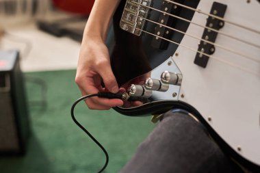 Elektro gitarda ses ve ton kontrollerini ayarlayan kişinin yakın görüntüsü, uygulama ortamında enstrüman düğmeleriyle el etkileşimine odaklanma