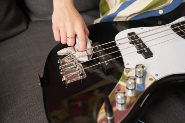 Koltukta elektrikli bas gitarı temizlerken ve korurken görülmüş. El kısmının yakın görüntüsü, temizlik sırasında perdelere ve dizgilere odaklanma