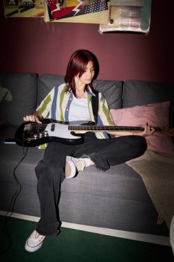 Bir kanepede oturup elektro gitar çalmak, rahatlama ve müzikal bağlılık göstermek, rahat, kapalı bir ortamda rahat bir ortam ve rahat bir ortam.