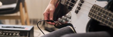 Performansa hazırlanırken kabloyu elektro gitara bağlayan kişi. Gitar ve amplifikatör belirgin bir şekilde sergilenmektedir, bu da müzikal oturum için kurulumu gösterir
