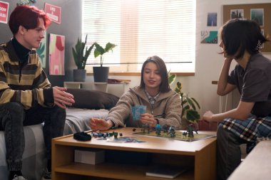 Evde ya da okulda birlikte fantezi oyunu oynayan üç ergen kız grubu ve zar atan gülümseyen kıza odaklanıyorlar.