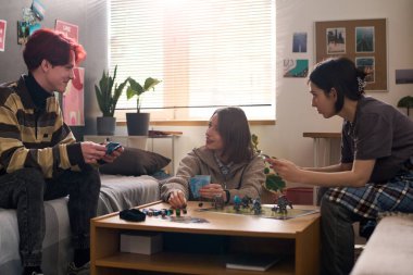 Üç gülümseyen genç birlikte masa başı oyunu oynamaktan ve masa fotokopisi alanındaki parçaları taşımaktan zevk alıyor.