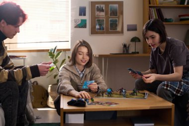 Evde ya da okul yurdunda arkadaşlarıyla masa başında oyun oynayan gülümseyen genç kız portresi.