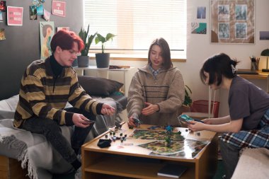 Yurt odasında masa oyunu oynayan üç genç arkadaştan oluşan gizli bir fotoğraf.