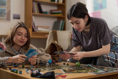 Masada arkadaşlarıyla oyun oynarken elinde kartlara bakan bir gencin portresi.