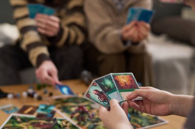 Arkadaşlarıyla masa oyunu oynarken elinde fantezi karakterleriyle oyun kartları tutan tanınmayan çocukları kapat