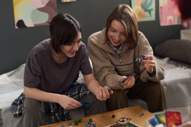 Masa oyunu oynayan ve içeride eğlenirken oyun taşlarını tutan iki genç kıza yüksek açılı bakış açısı