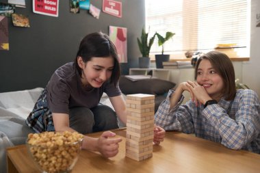 Evde ya da okul yurdunda oyun oynarken iki genç kızın ahşap kule oynayıp gülümsediği samimi bir an.