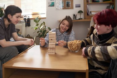 Yurt odasında oyun oynarken ve ahşap kuleyi dengelerken üç genç arkadaşın mutlu bir şekilde güldüğü bir grup.