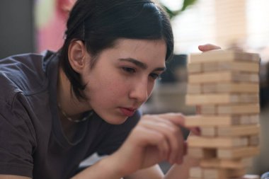 Dikkatle odaklanmış genç kızın portresini kapat. Ahşap kuleden bloğu dikkatlice kaldırırken arkadaşlarıyla oyun oynarken yoğun yüz ifadesi takınıyor.