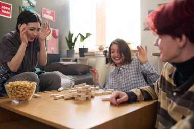 Üç genç arkadaşın, ahşap blok kulesi yıkılırken, yurt odasında oyun oynarken ve birlikte eğlenirken duygusal tepki verdiği samimi an.
