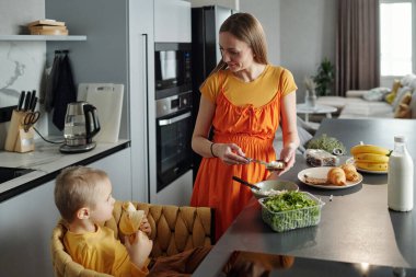Anne ve oğlunun sabah rutin mutfak sahnesinde sağlıklı bir kahvaltı hazırlarken yüksek açılı görüntüsü.