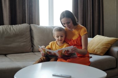 Oturma odasında kanepede otururken anne ve çocuğun resim kitabı okuduğu gizli bir sahne.